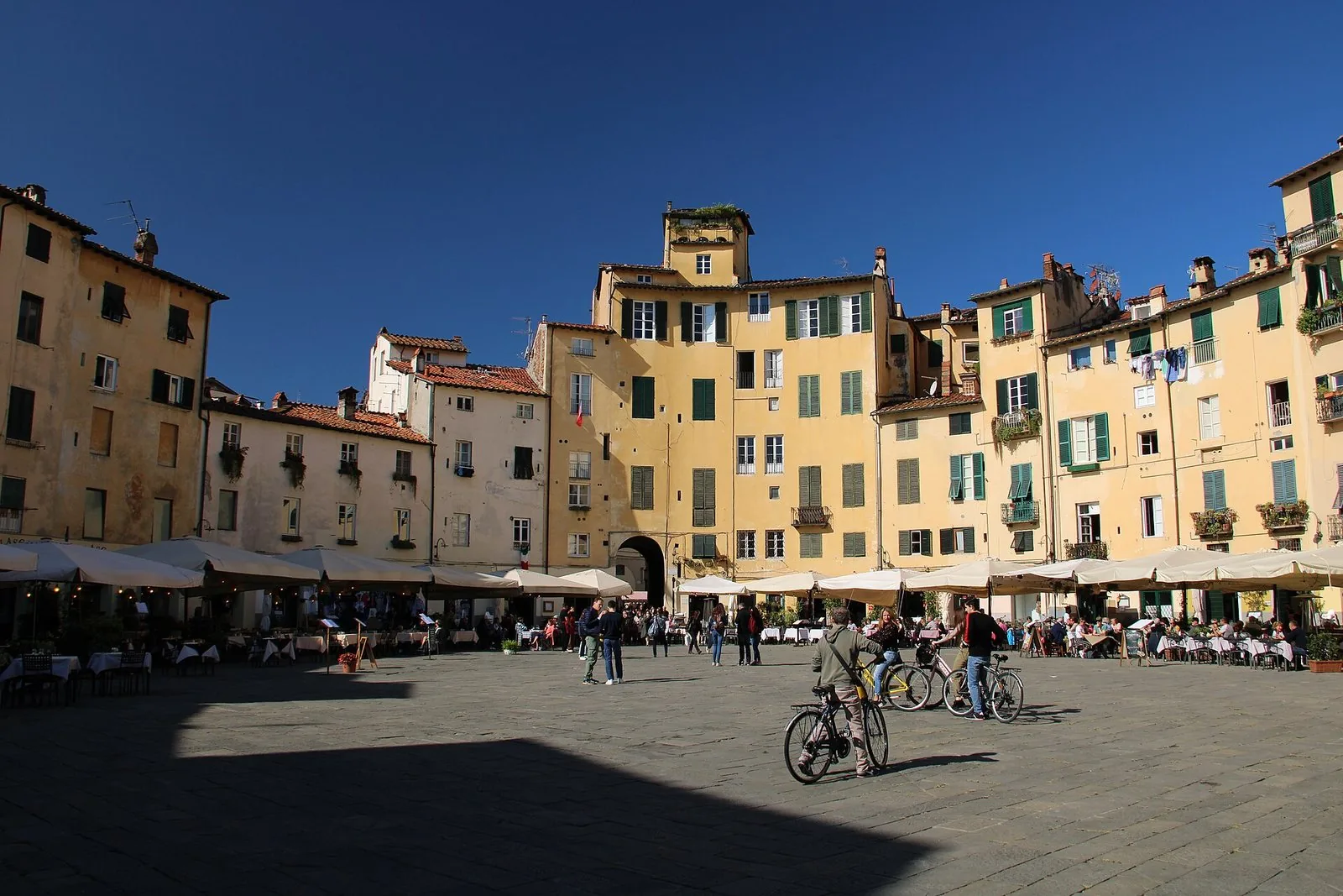 Piazza dell'Anfiteatro a Lucca con le facciate gialle delle case in cerchio e i tavolini all'aperto